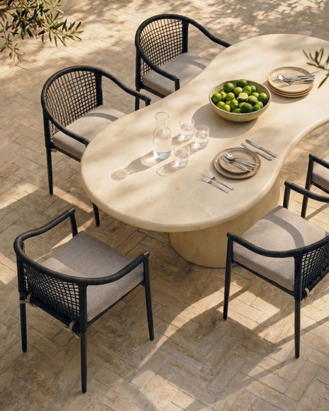Moderner Gartentisch in Ovalform aus Steinoptik mit vier schwarzen Seilgeflecht-Armlehnenstühlen auf einer sonnigen Terrasse.