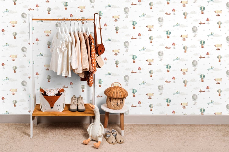 Kinderzimmer mit Kleiderständer, Kleidung, Spielzeug und Tapete mit Luftballonmuster