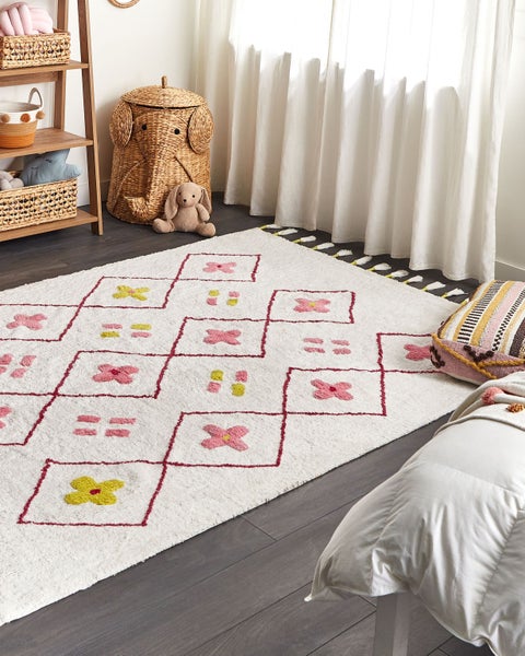 Hell eingerichtetes Kinderzimmer mit einem Hochflor-Teppich mit geometrischem Muster, Blumenmotiven und Quasten, Holzregal und Elefanten-Korb.