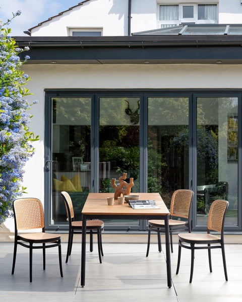 Gartenszene mit Holztisch und Rattanstühlen vor einem Haus