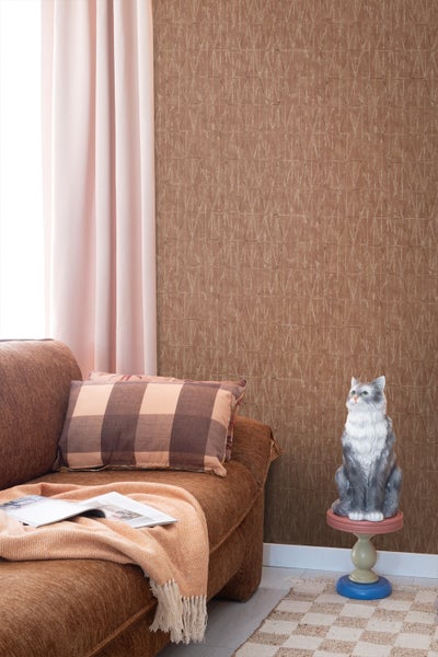 Wohnzimmer mit braunem Sofa, kariertem Kissen, Dekofigur Katze und gemusterter Tapete