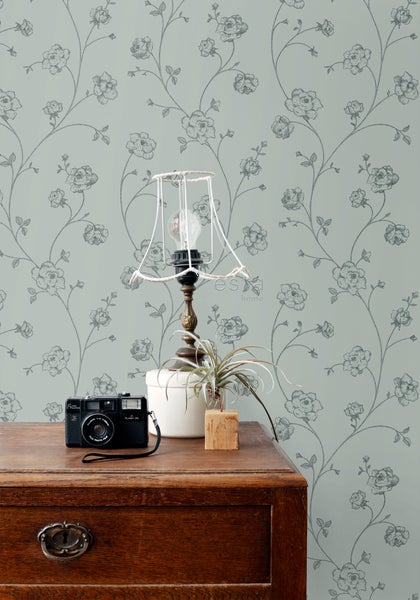 Dekoratives Zimmer mit Blumendrucktapete, Holztisch, Lampe und Kamera.