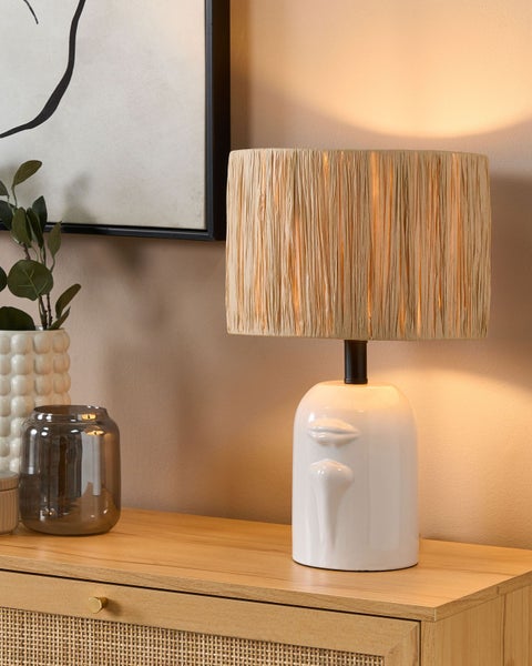 Tischlampe mit Gesicht und Lampenschirm aus Bast auf einem Holzschrank