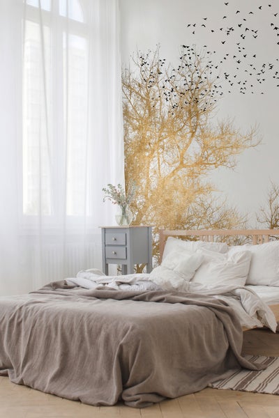 Helles Schlafzimmer mit Fototapete eines goldenen Baums und fliegenden Vögeln, Holzbett und grauem Nachttisch.