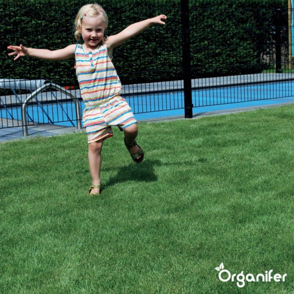 Ein Kind balanciert auf einer dichten Rasenfläche im Garten. Im Hintergrund ein Pool und Zaun. Organifer Logo.
