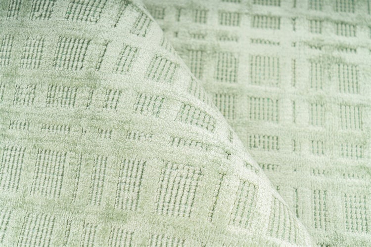 Hellgrüner Teppich mit geometrischem Karomuster und weicher Oberflächenstruktur in einer Detailaufnahme.