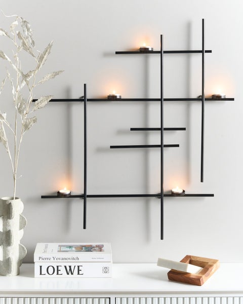 Wandkerzenhalter aus Metall mit Teelichtern und dekorativen Elementen auf einer Kommode