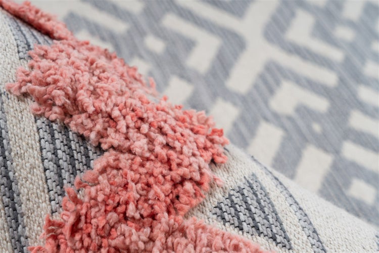 Detailansicht eines Teppichs mit rosa Hochflor-Elementen und grau-weißem geometrischem Webmuster.