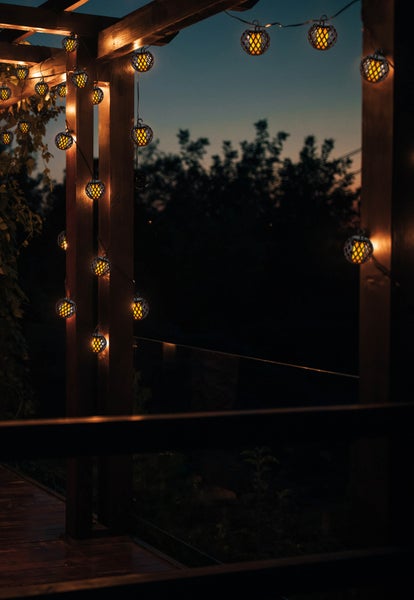 Lichterkette mit kugelförmigen Laternen, die an einer Holzpergola hängen und abends ein warmes Licht verbreiten.