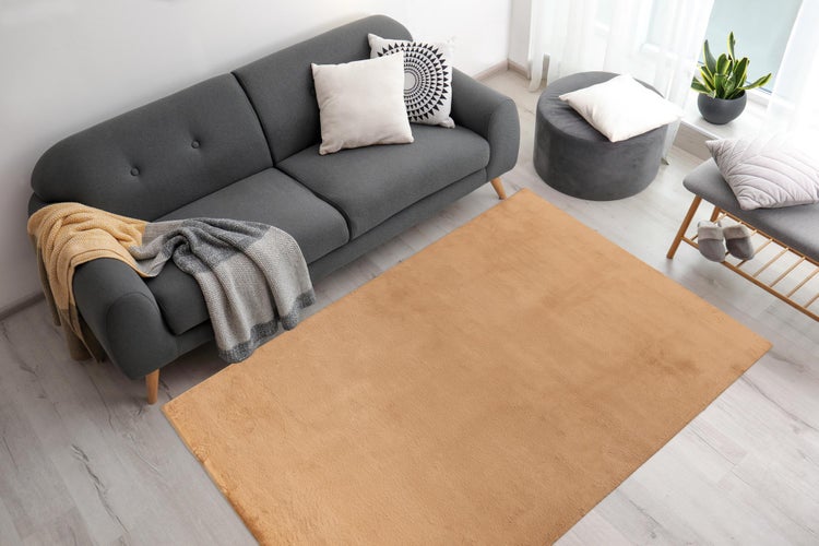 Moderner Wohnbereich mit dunkelgrauem Sofa, Zierkissen, Decke und einem senfgelben rechteckigen Teppich auf hellem Holzboden.