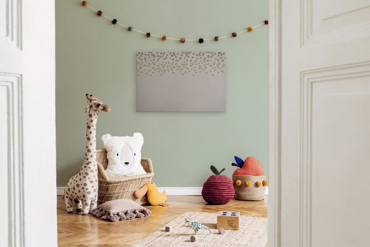 Ein Kinderzimmer mit einem Wandbild mit Punktemuster, einer Giraffenfigur, einem Rattansessel und Spielzeug auf einem Holzboden.