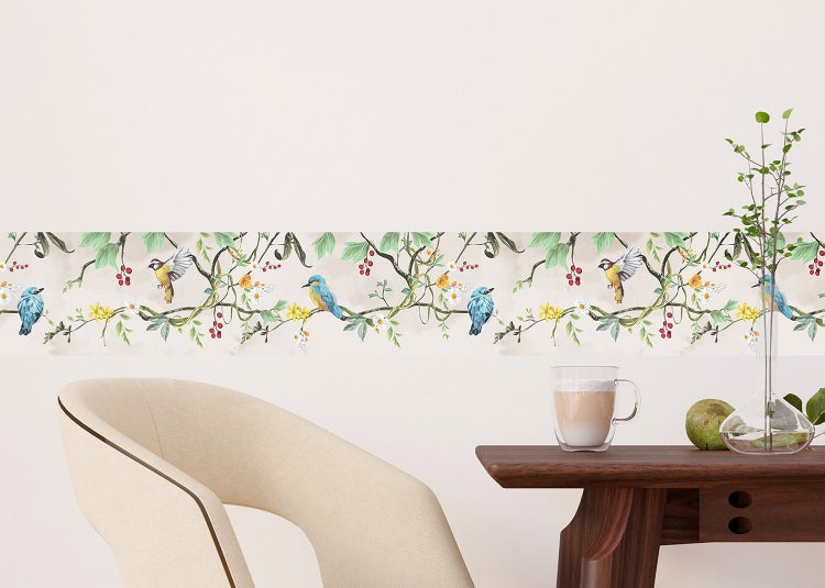 Tapetenbordüre mit Naturmotiv aus Vögeln, Zweigen und Blüten an einer Wand über einem Tisch und einem Stuhl.