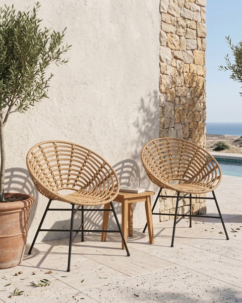 Zwei runde Loungesessel aus Korbgeflecht mit Metallbeinen und einem kleinen Holztisch auf einer Terrasse mit Natursteinmauer.