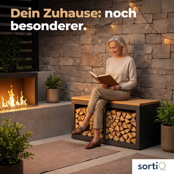 Eine Frau liest auf einer Holzbank, die mit Brennholz gefüllt ist, neben einem Kamin und Pflanzen.