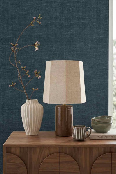 Dunkelblaue Tapete mit Textilstruktur hinter einer Holzkommode mit Tischleuchte, Vase und Dekoration im Wabi-Sabi-Stil.