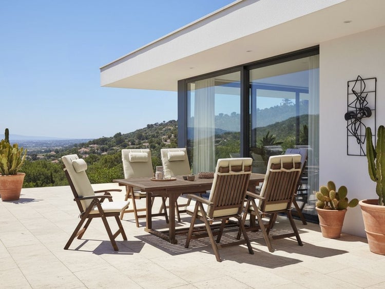 Gartenszene mit Esstisch und Stühlen auf einer Terrasse mit Blick auf eine grüne Hügellandschaft