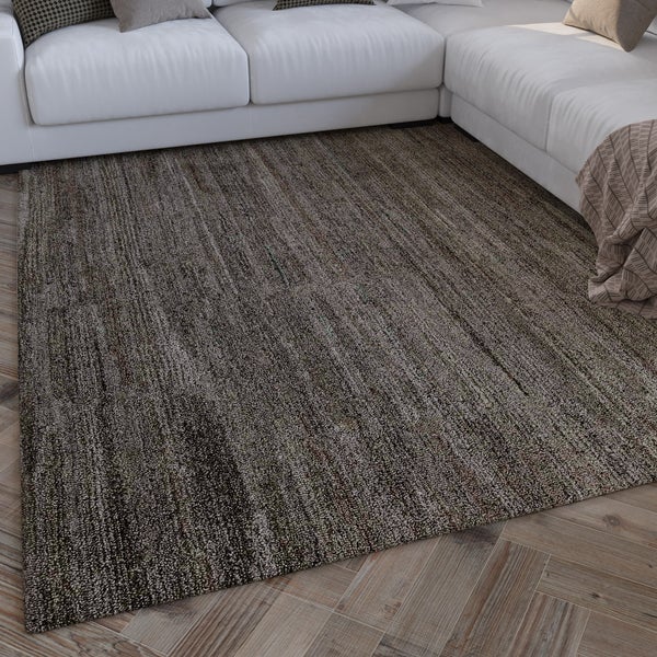 Strukturierter Teppich in melierter Optik vor einem Sofa auf Fischgrät-Parkett im Wohnzimmer.