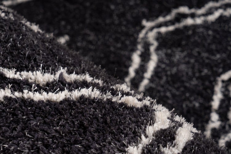 Detailaufnahme eines schwarz-weißen Hochflor-Teppichs mit wellenförmigem Muster und weicher Struktur.