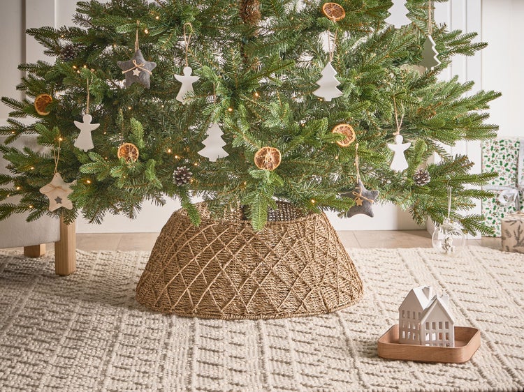 Dekorierter Weihnachtsbaum mit geflochtenem Baumständer auf einem Teppich