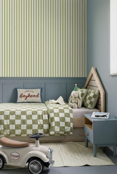 Kinderzimmer mit Hausbett aus Holz, karierter Bettwäsche, gestreifter Tapete, blaugrauer Wandpaneele und einem Vintage-Spielzeugauto.