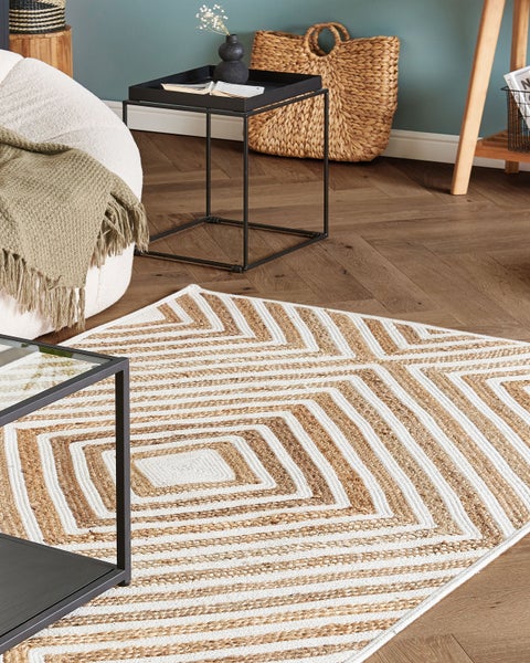 Teppich mit geometrischem Rautenmuster auf Holzparkett in einem hellen Wohnzimmer mit Beistelltisch und Sitzgelegenheit.