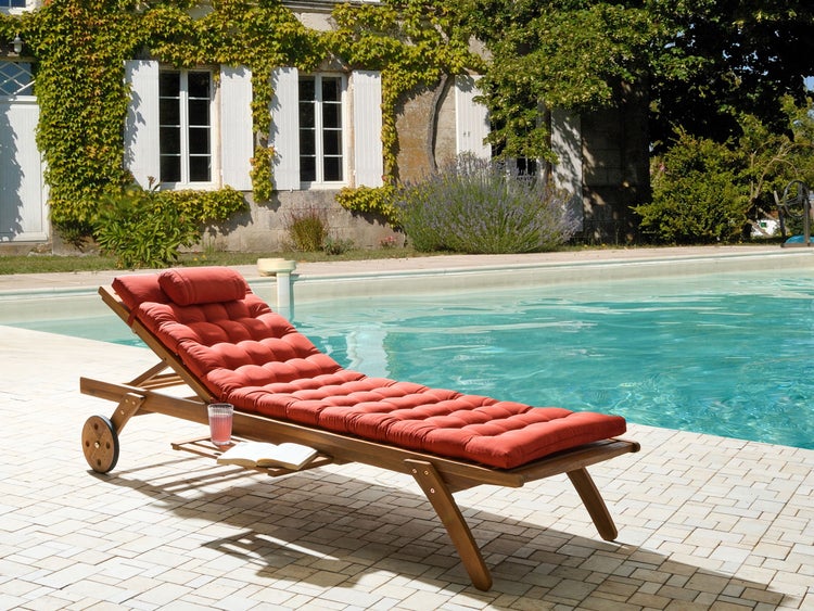 Holzliege mit roter Auflage am Pool