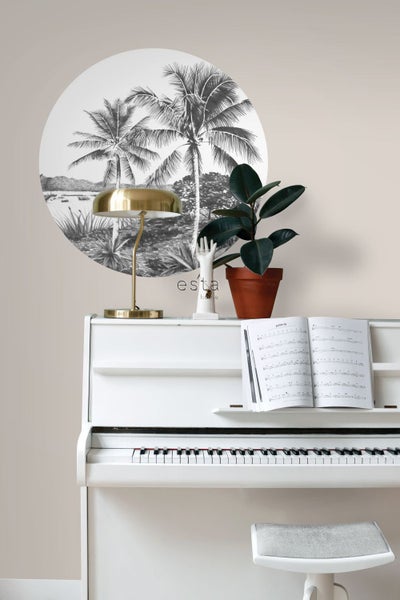 Szene mit einem weißen Klavier, einer goldenen Lampe, einer Zimmerpflanze und einer runden Wanddekoration mit einem Palmenmotiv.