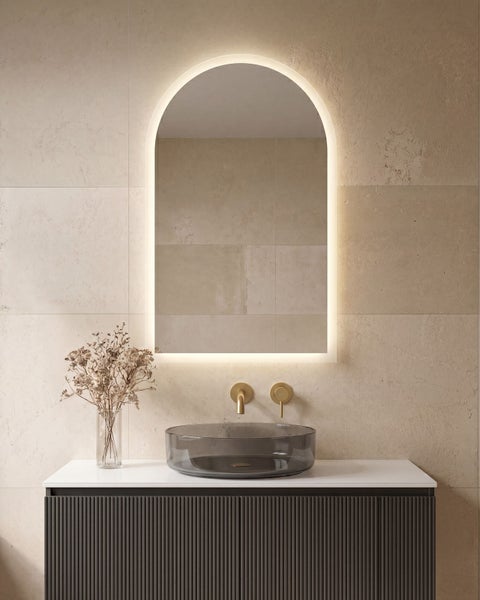 Modernes Badezimmer mit bogenförmigem Spiegel mit Beleuchtung, Glaswaschbecken auf strukturiertem Unterschrank und Wandarmatur.