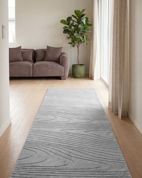 Langer Läufer mit strukturiertem Wellenmuster in einem hellen Wohnzimmer mit Holzboden, braunem Sofa und Zimmerpflanze.