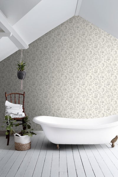 Helles Badezimmer mit floraler Mustertapete, freistehender Badewanne, Holzstuhl mit Handtüchern und Pflanzen auf weißem Holzboden.