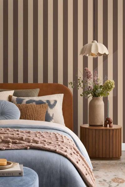 Schlafzimmer mit gestreifter Tapete, Veloursbett und Nachttisch mit Blumenvase und Hängelampe für eine gemütliche Einrichtung.