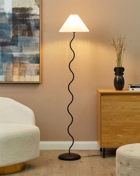 Eine Stehlampe mit plissiertem Schirm und gewundenem Ständer in einem hellen Wohnraum.