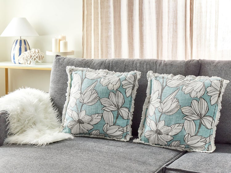 Graues Sofa mit zwei türkisfarbenen Kissen mit Blumenmuster und Fransen