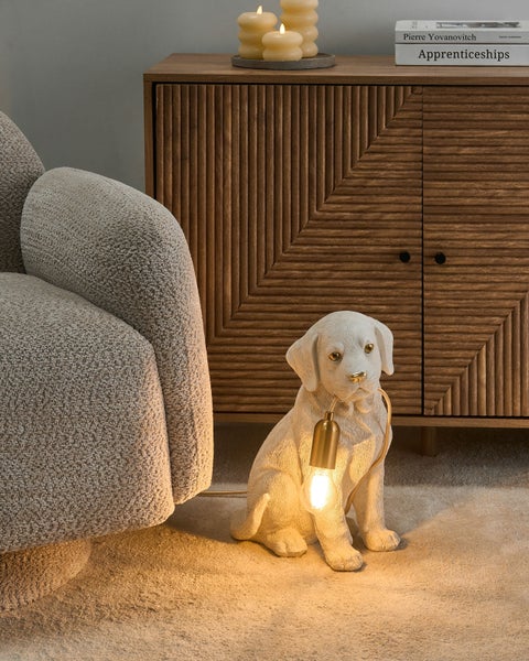 Tischleuchte in Form eines sitzenden Hundes, der ein Leuchtmittel im Maul hält, in einem modern eingerichteten Wohnzimmer.