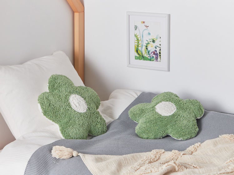 Zwei grüne, blütenförmige Kissen auf einem Bett mit einer grauen Tagesdecke.