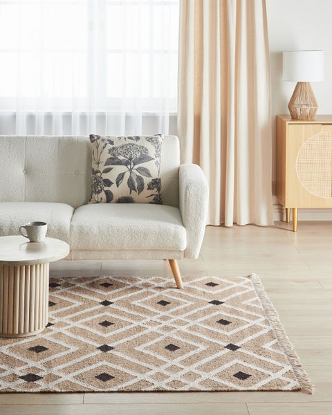 Modernes Wohnzimmer mit Bouclé-Sofa, Kissen mit Blumenmuster, Teppich mit Rauten, rundem Holz-Couchtisch und Sideboard aus Holz.