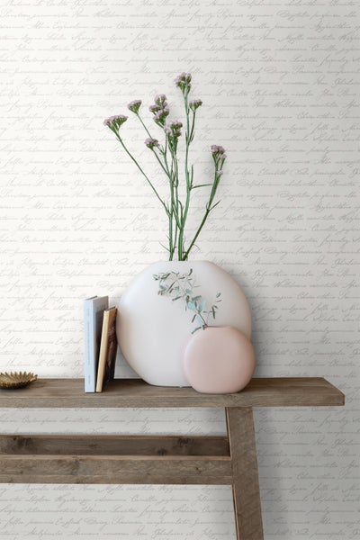 Dekorative Szene mit Vasen, Blumen, Büchern und einem Holzbord vor einer Wand mit Schriftzugmuster