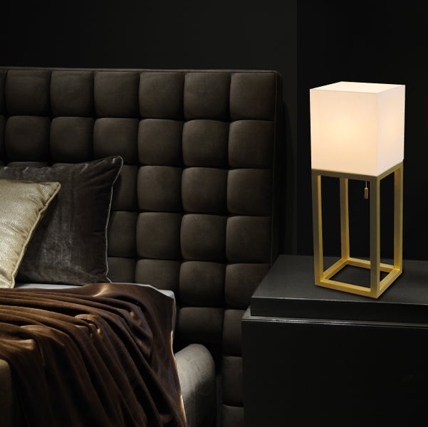 Nachttischlampe mit quadratischem Lampenschirm und goldenem Gestell neben einem Bett mit gestepptem Kopfteil