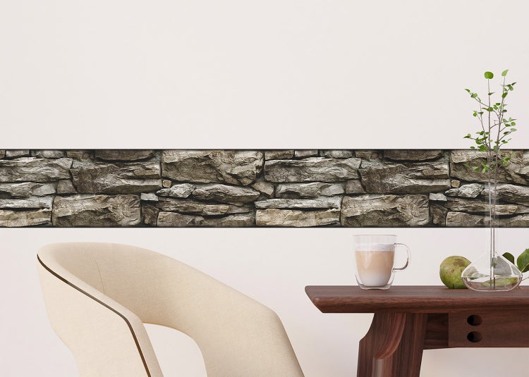 Selbstklebende Tapetenbordüre in Steinoptik an einer Wand in einem modern eingerichteten Raum mit Tisch und Stuhl.