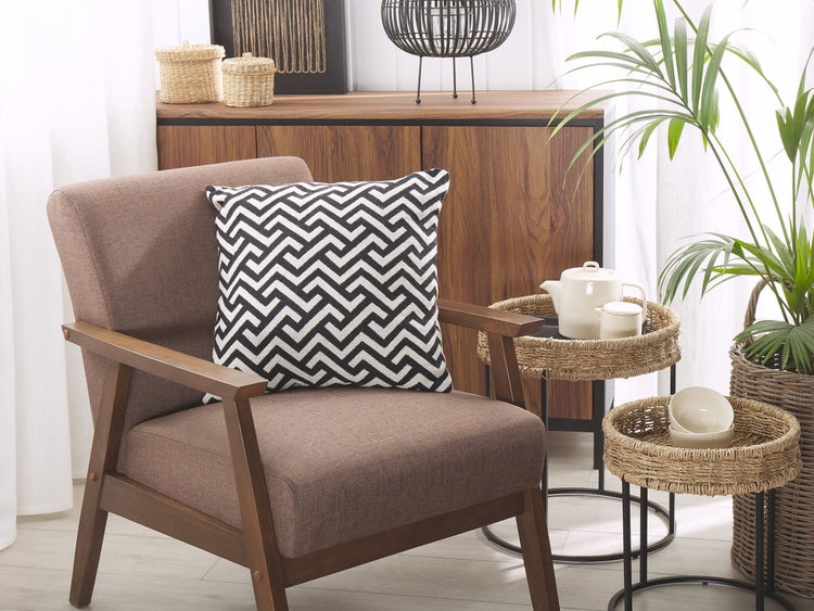 Wohnzimmerszene mit Sessel, Kissen, Beistelltischen, Geschirr und Pflanze.