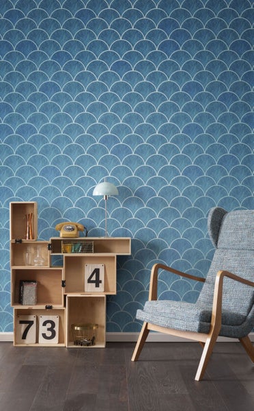 Szene mit einer blauen Tapete mit Muster, einem Holzregal und einem Sessel