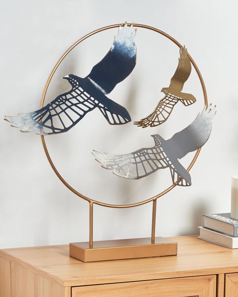 Dekorative Metallskulptur mit Vogeldarstellung in einem goldenen Kreis auf einem Holzmöbelstück.