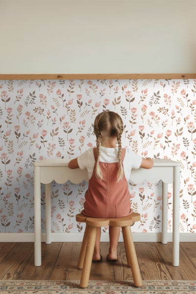 Mädchen sitzt an Kindertisch vor einer floral gemusterten Tapete