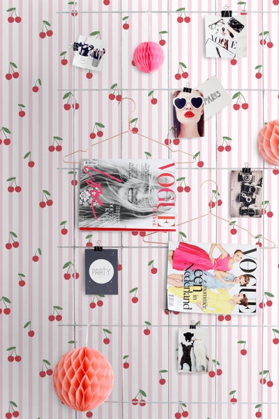 Dekorative Wand mit Kirschmuster, Drahtgitter und daran befestigten Zeitschriften, Fotos und Papierdekorationen.