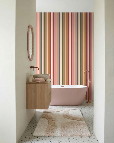 Modernes Badezimmer mit bunt gestreifter Tapete, rosa freistehender Badewanne, hölzernem Waschtisch und Terrazzoboden.