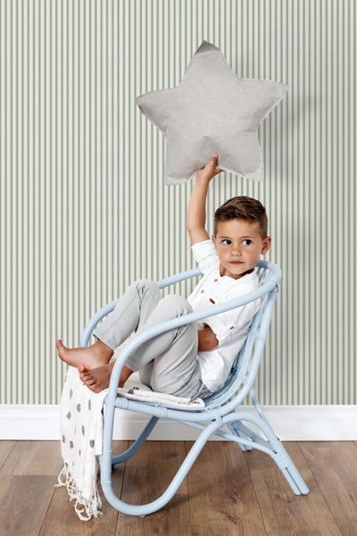 Ein Junge sitzt in einem blauen Korbsessel und hält ein Sternkissen hoch, vor einer gestreiften Tapete.