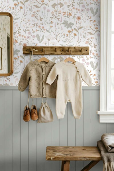 Tapete mit floralem Wiesenmuster in einem Kinderzimmer mit Holzpaneelen und an der Wand hängender Babykleidung.