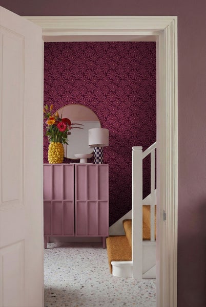 Blick durch eine offene Tür auf einen Flur mit Kommode, Spiegel, Lampe, Blumenvase, Tapete und Treppe.