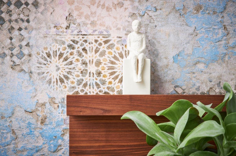 Dekorative Figur auf einem Sockel vor einer gemusterten Wand