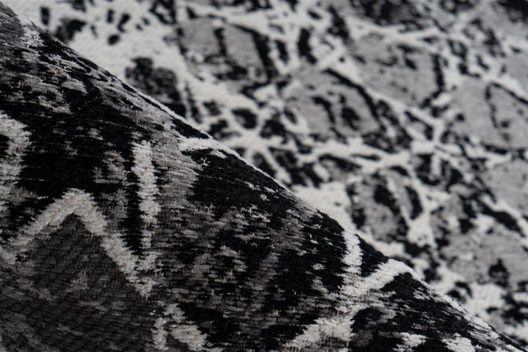 Detailaufnahme eines Teppichs mit abstraktem Muster in Schwarz, Weiß und Grau mit gewebter Struktur.